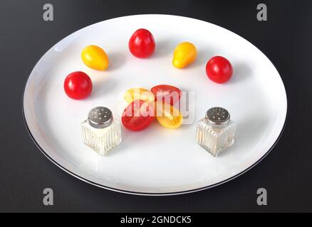 A few cocktail tomatoes with salt and pepper, arranged on a white plate. Stock Photo
