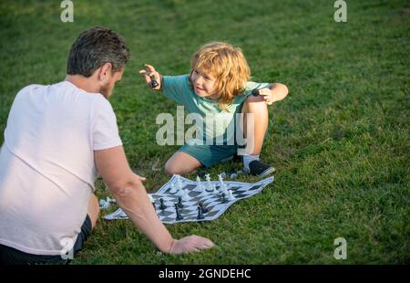 happy family of father and son boy playing chess on green grass in park outdoor, chess game Stock Photo