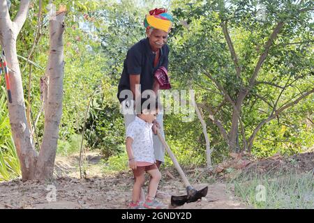 Close-up of Indian grandfather younger grandson working in the garden with a shovel and younger grandson watching grandfather's actions Stock Photo
