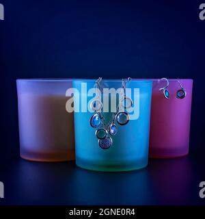 A colorful bracelet and earrings hanging from glass candle holders on blue background Stock Photo