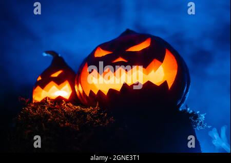 Two glowing lanterns are orange-blue scary pumpkins with smoke forest. Stock Photo
