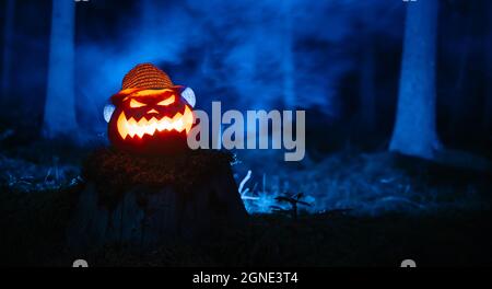 Creepy carved pumpkin for Halloween with blue smoke in the forest. Stock Photo
