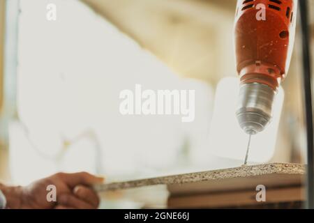 Carpenter drilling a hole in a sheet of chipboard, using a handheld electric drill in a low angle close up on the wood and drill bit - artistic blur Stock Photo