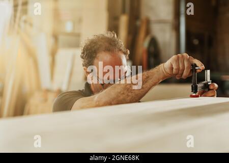 Carpenter adjusting a clamp on a plank of wood in a woodworking workshop of factory in a low angle view across the timber with copyspace Stock Photo