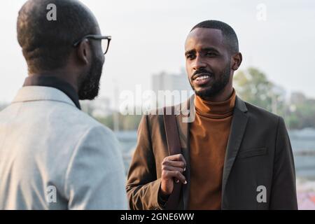 Horizontal over-the-shoulder shot of handsome young African American man standing in front of his co-worker discussing something during break Stock Photo