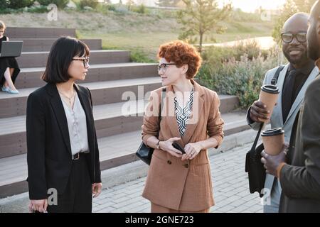 Group of modern business people standing together in urban park relaxing, drinking coffee and talking to each other during coffee break Stock Photo