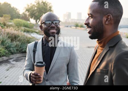 Selective focus shot of young adult African American man spending time outdoors with his colleague drinking coffee and chatting Stock Photo