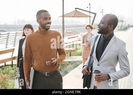 Horizontal medium shot of two African American men walking together along street talking about something after finishing workday in office Stock Photo