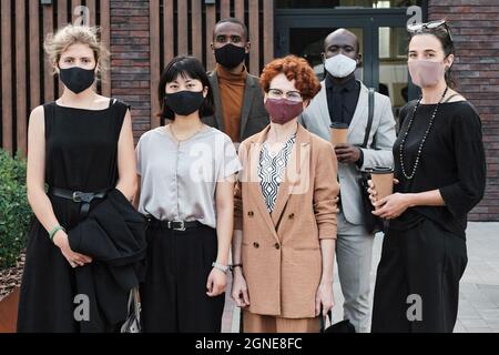 Horizontal medium long group portrait shot of unrecognizable multi-ethnic men and women wearing protective masks on faces looking at camera Stock Photo