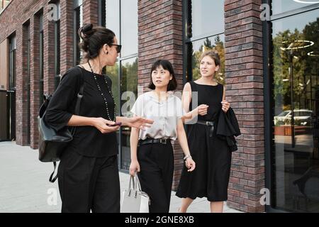 Group of three stylish multi-ethnic women walking along business district sharing ideas about new project Stock Photo