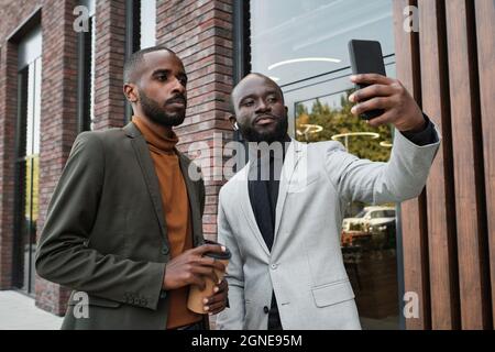 Horizontal medium portrait shot of two modern handsome Black men standing outdoors having fun taking selfie photos on smartphone camera Stock Photo