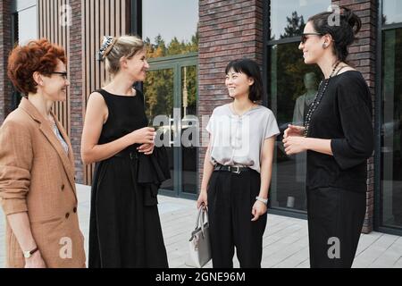 Group of four charming multi-ethnic women spending break time together standing outdoors having interesting conversation Stock Photo