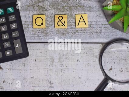 Top view of calculator and magnifying glass with Q and A written on wooden blocks. Copy space. Selective focus. Stock Photo