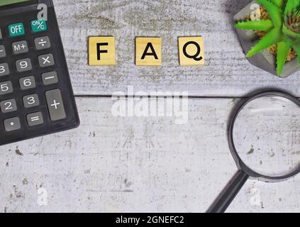 Top view of calculator and magnifying glass with FAQ written on wooden blocks. Copy space. Selective focus. Stock Photo