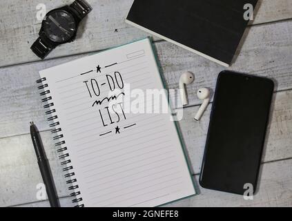 TO DO LIST text on notebook surrounded by watch, smartphone, pen and wireless earphones. Selective focus Stock Photo