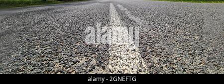 White dividing strip painted on asphalt road against background of trees and blue sky Stock Photo