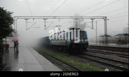 A goods train passes from the Sahibabad railway station during the monsoon rain near New Delhi Railway station, India. Stock Photo