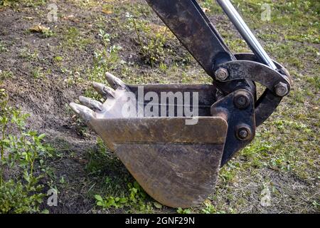 Bucket of small excavator is located on lawn. Strong teeth are ready to bite into the ground. Copy space. Close-up. Selective focus. Stock Photo