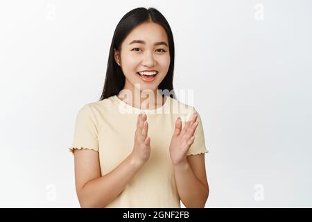 Close up of happy asian girl applause, clap hands and smiling, praise something good, standing over white background Stock Photo