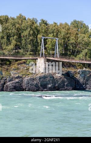 A suspension bridge over a wide river in the mountains.  Stock Photo
