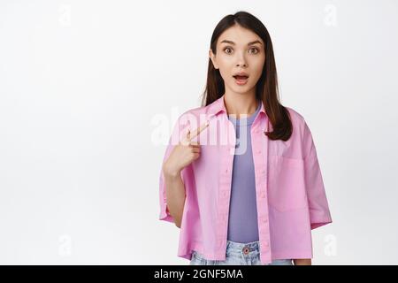 Image of girl looks surprised, points at herself, being chosen, shocked to win smth, stands against white background Stock Photo