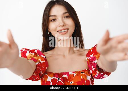 Close up portrait of beautiful brunette woman reaching hands, stretching out arms to hold camera, hugging you, standing over white background Stock Photo