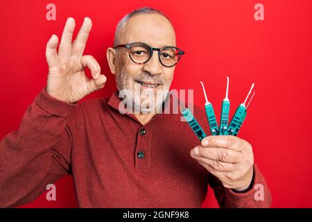 Handsome mature man holding picklock to unlock security door doing ok sign with fingers, smiling friendly gesturing excellent symbol Stock Photo