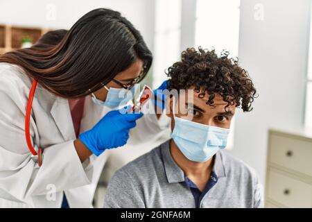 Young latin doctor woman auscultating the ear of man using otoscope at examination room. Stock Photo