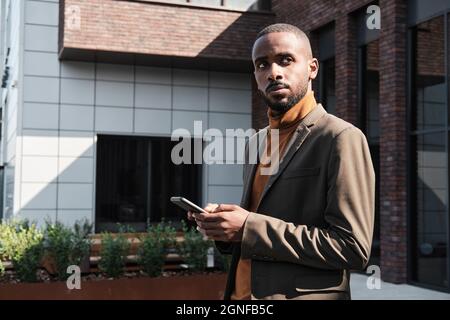 Horizontal medium portrait of handsome African American man with beard on face wearing stylish suit and turtleneck sweater standing outdoors Stock Photo