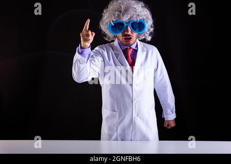 Angry science teacher in white coat with unkempt hair in funny eye glasses with the raised finger Stock Photo