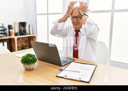 Senior man working at the office using computer laptop suffering from headache desperate and stressed because pain and migraine. hands on head. Stock Photo
