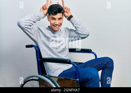 Young hispanic man sitting on wheelchair posing funny and crazy with fingers on head as bunny ears, smiling cheerful Stock Photo