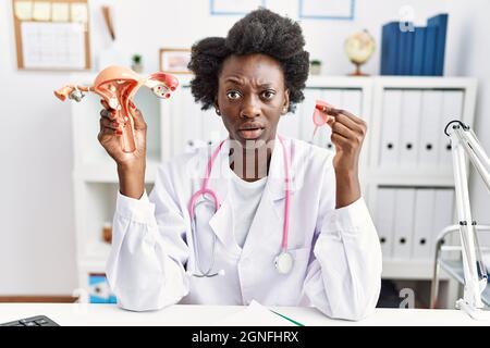 African doctor woman holding anatomical female genital organ and menstrual cup clueless and confused expression. doubt concept. Stock Photo