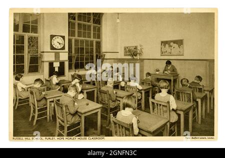 1930's era by Bedford Lemere & Co.  postcard of primary school children, sitting at desks with knitting wool, with teacher, Hope Morley House Classroom, large clock on the wall, Russell Hill School - a boarding school,  Purley, London, England, U.K. Stock Photo