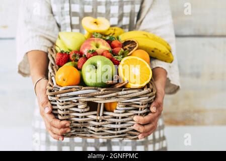 Hands of woman holding wicker basket full of colorful mixed fruit in abundance. Woman with variety of healthy fruit in basket. Fresh fruit collection Stock Photo