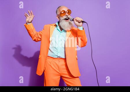 Photo of old funny dreamy cool man sing karaoke mic wear sunglass isolated on purple color background Stock Photo