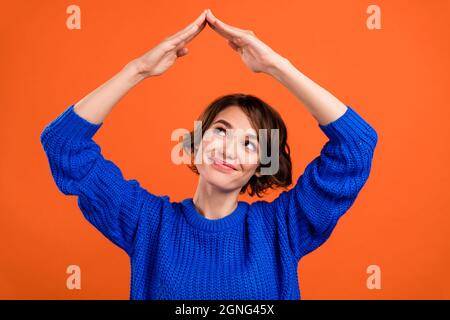 Photo of nice brunette short hairdo young lady look hands roof wear blue sweater isolated on orange color background Stock Photo
