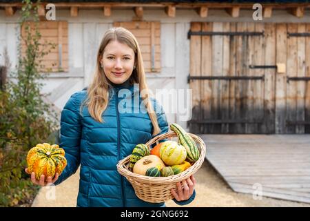 A girl in a household yard with a basket in her hands filled with fresh vegetables, in one hand holds a pumpkin and in the other holds a basket with v Stock Photo