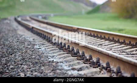 Selective focus railway track turns and twists between out of focus hills background. Empty rounding and turning single track of railways. Shallow Stock Photo
