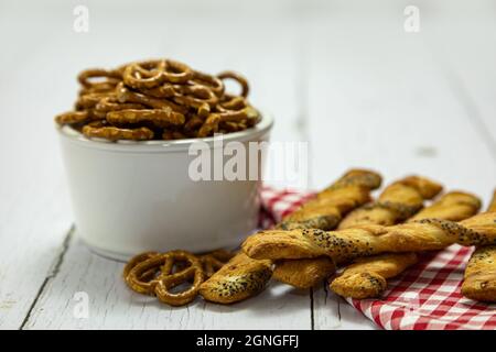 Breadsticks and bowl of salted pretzel snacks with red check napkin on white wooden table Stock Photo