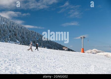 Kalavrita ski Resort, Greece - December, 31 2019: Two happy girls running down in snowy slope enjoying winter holidays at ski resort in Greece. Kids h Stock Photo