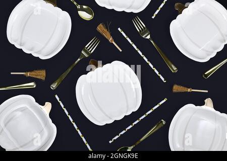 Elegant Halloween party flat lay with pumpkin shaped plates, brooms and golden forks and spoons on black background Stock Photo