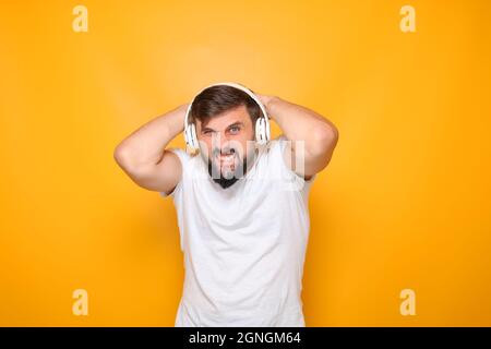 bearded man clutched his head in despair and listens to music on headphones.
