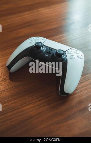 London, UK - May 25, 2021: White Playstation 5 (PS5) wireless controller on a wooden table, selective focus. Playstation 5 is the latest video game co Stock Photo