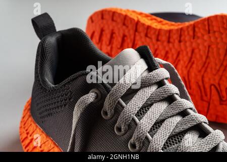 Elastic laces of gray mesh fabric sneakers with orange grooved sole close-up. Lacing up the modern textile trainers for sport and active lifestyle. Stock Photo