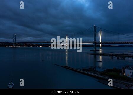 South Queensferry, Eaglesham, Scotland, UK. 25th Sep, 2021. PICTURED: Night aerial drone view of Forth bridges. Forth Road Bridge seen with no traffic on it. Since a crack was discovered in part of the bridges structure and subsequently repaired, the bridge had seen light traffic, with the new Queensferry Crossing being built, which now takes the majority of vehicles, the Forth Road Bridge still takes busses and taxis. Credit: Colin Fisher/Alamy Live News Stock Photo