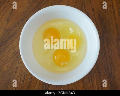 Three eggs in a white bowl on a wood table Stock Photo