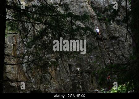 A woman climbing with a rope secured by a friend. Going down the rocky cliff holding the rope Stock Photo