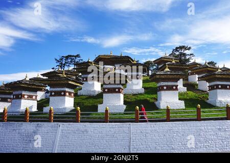 A lone woman in red walks past some of the 108 identical Druk Wangyal Chortens located at Bhutan’s Dochula Pass on the road from Thimphu to Punakha. Stock Photo