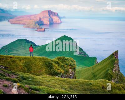 Lonely tourist admiring of sunset on Alaberg cliffs, Faroe Islands, Kingdom of Denmark, Europe. Colorful evening view of Mykines island with Vagar isl Stock Photo